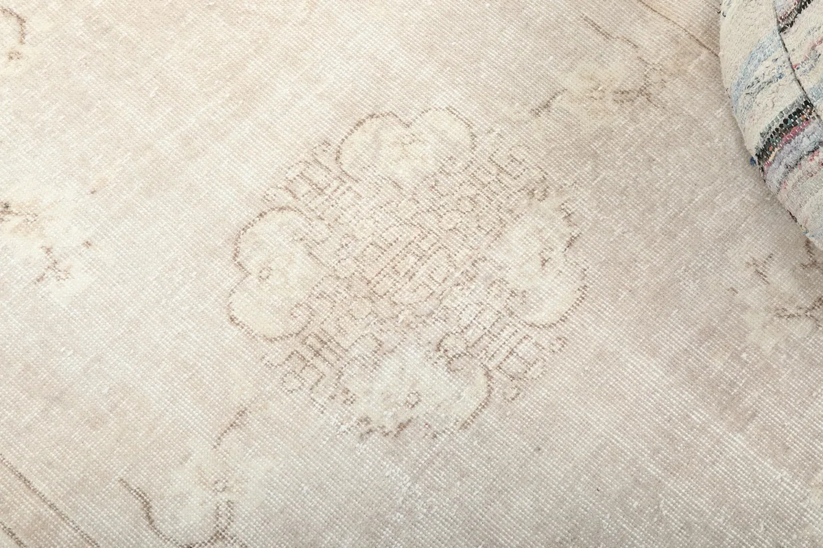 Detailed close-up of the central medallion motif on the beige hand-knotted wool rug.