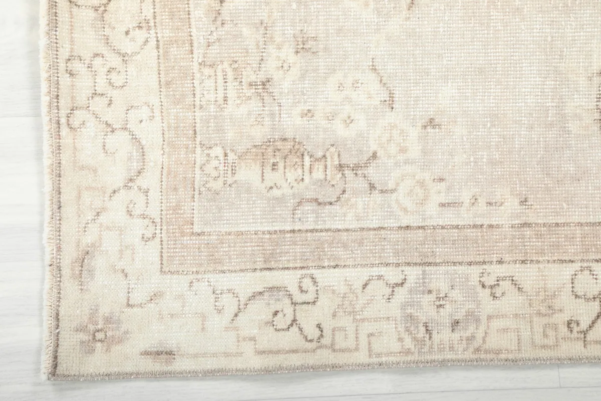 Close-up of the intricate border design and corner of the beige vintage wool rug.
