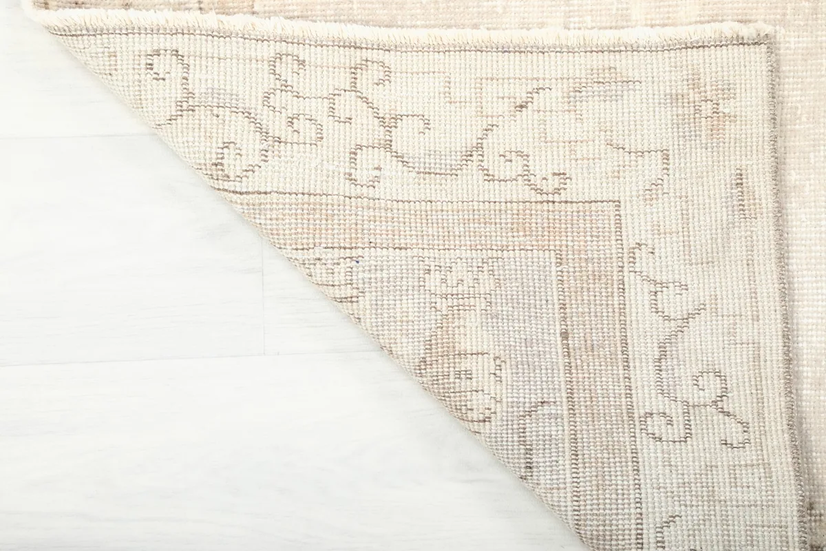 Underside corner of the beige rug, revealing the cotton foundation and hand-knotted construction.