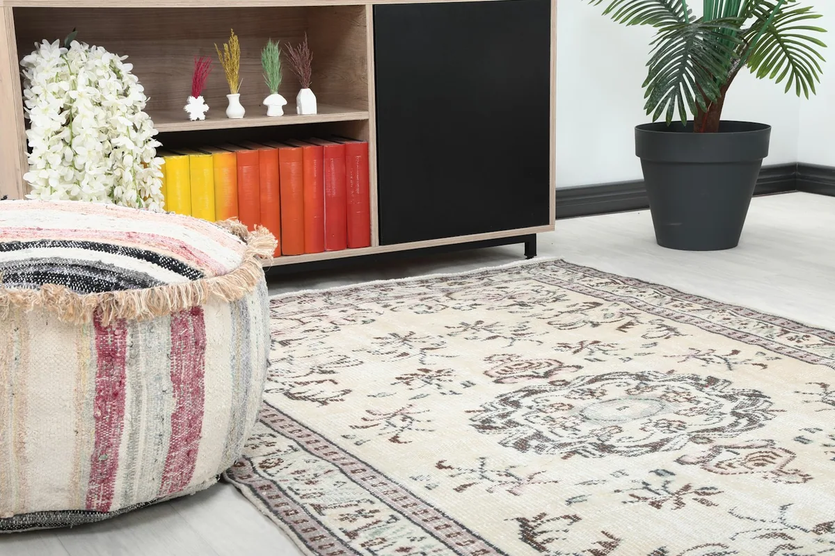 Close-up of the vintage rug's corner next to an ottoman and shelving unit in a room.