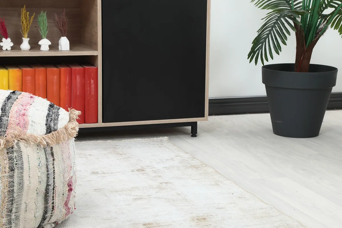 Close-up view of the cream runner rug on light flooring, next to a colorful ottoman and bookshelf.