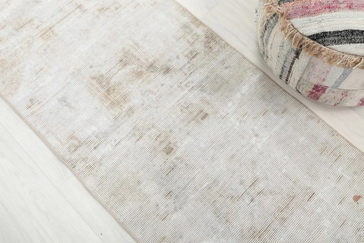 Detailed view of the distressed cream and tan wool pile with faded geometric patterns on the runner rug.