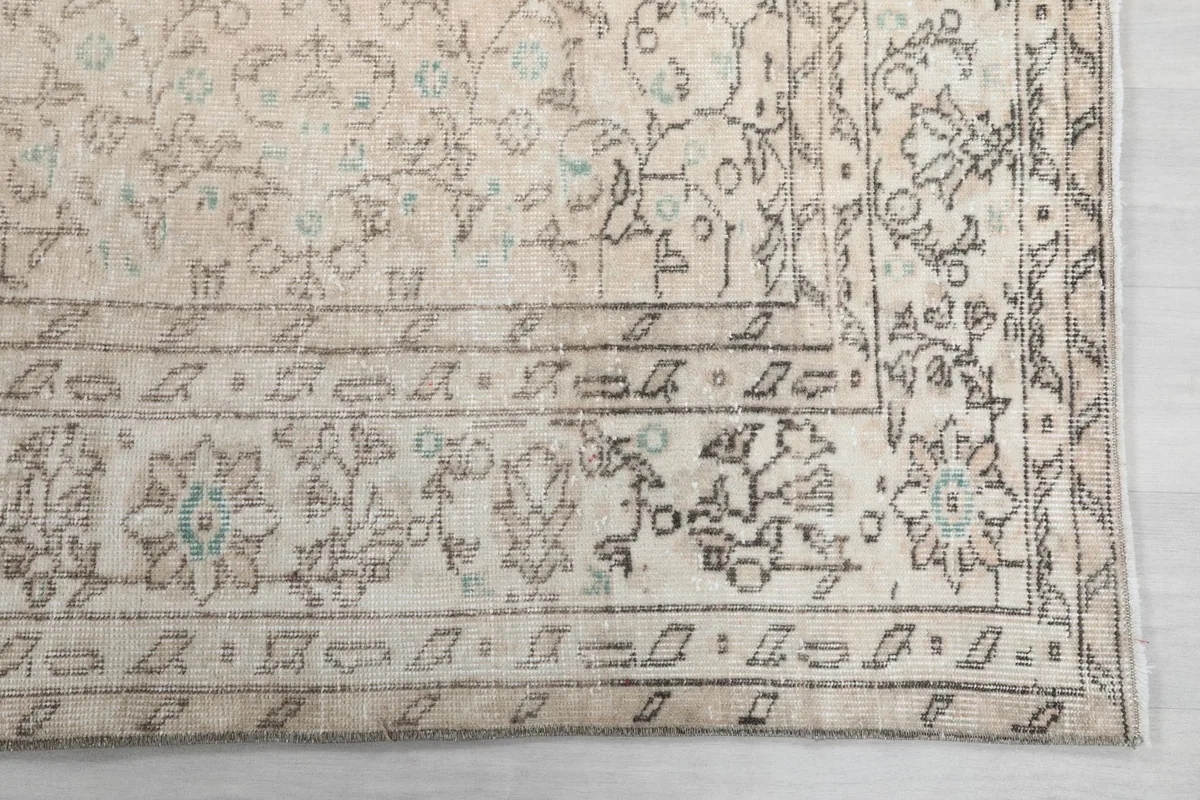 Detail of the rug's border, featuring a gray floral design against the cream background with hints of blue.