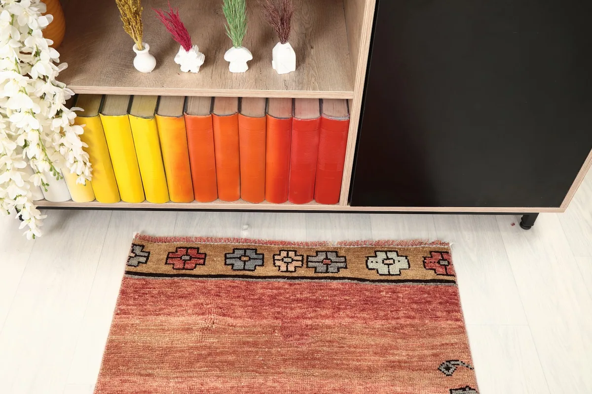 Detail of one end of the runner rug in a room, showing the border design and a bookshelf.