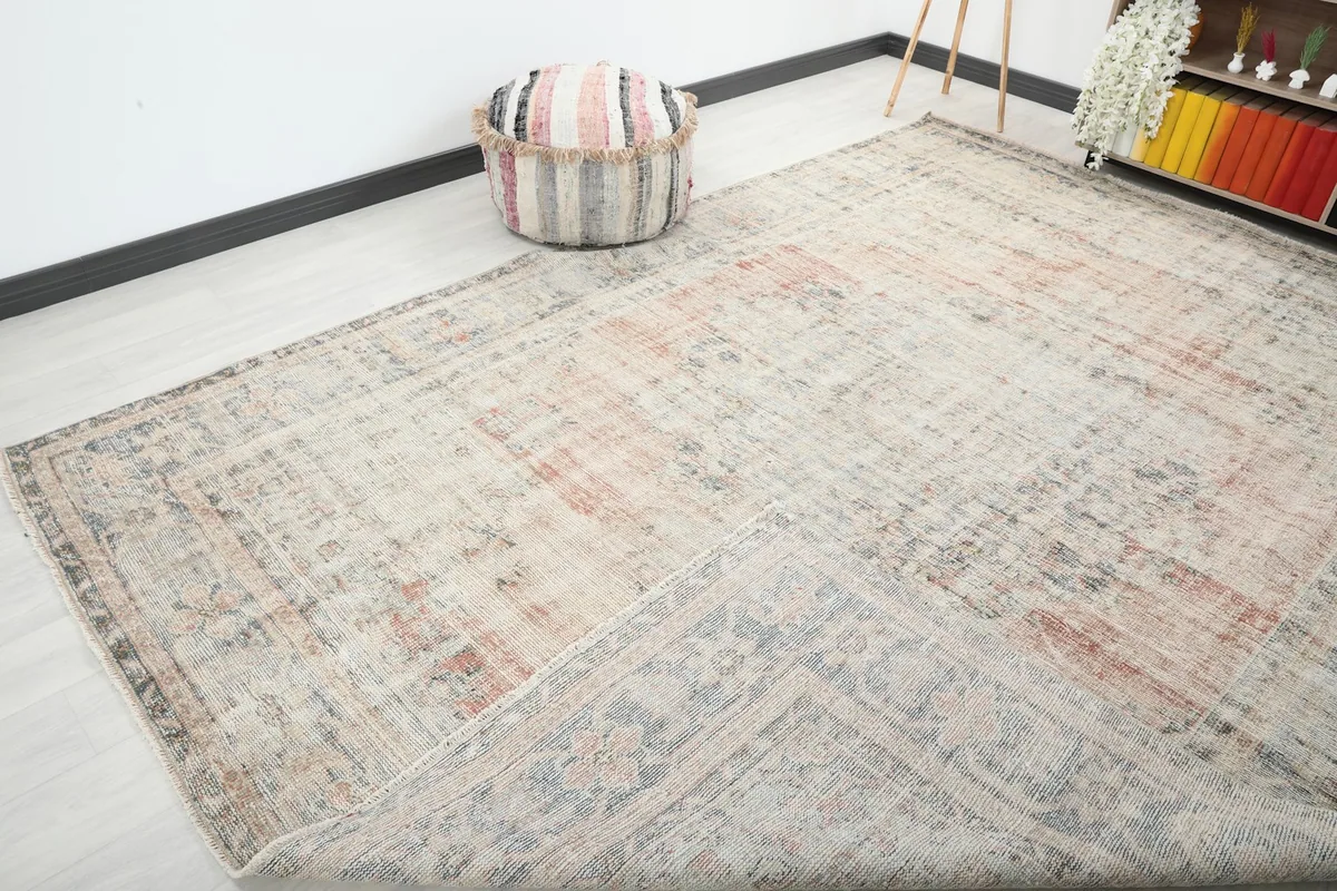 Angled view of the large vintage rug, highlighting its distressed appearance and colors