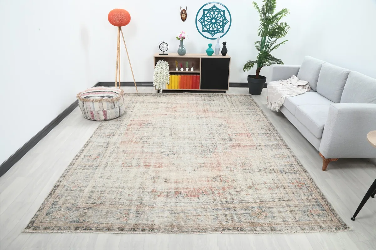 Large ivory and rose vintage rug displayed in a living room setup with a gray sofa