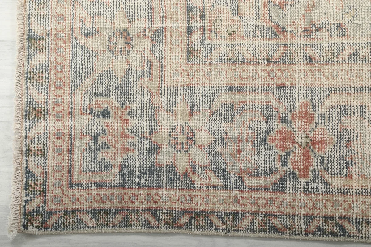 Corner detail showing the faded blue and brown border patterns and ivory fringe