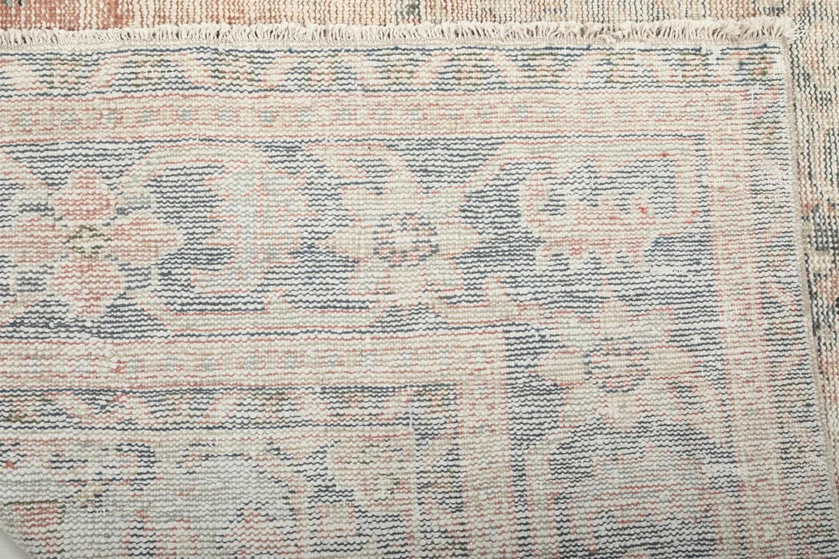 Close-up of the low wool pile and hand-knotted texture with faded blue and ivory threads