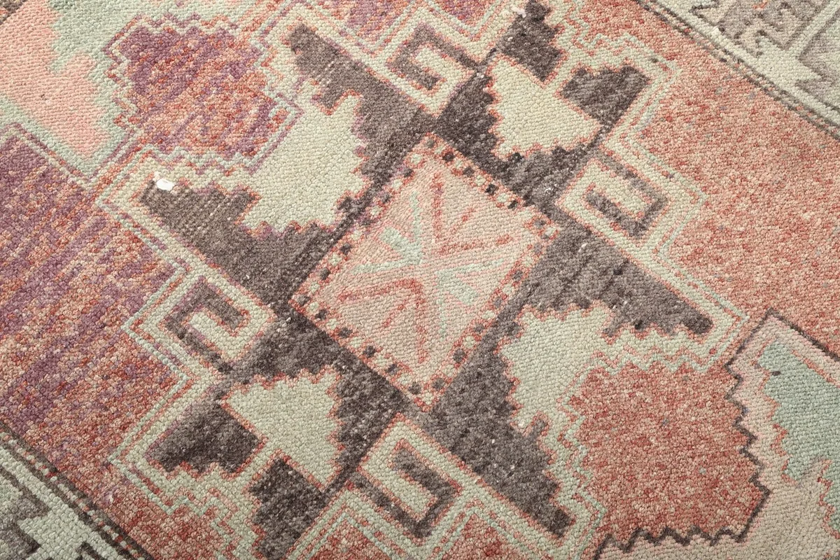Detailed view of a central geometric motif in rust, green, and black, showing the hand-knotted wool pile.