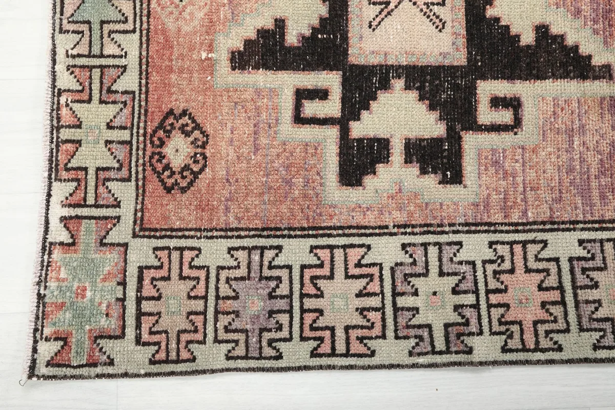 Close-up of the beige border and corner of the rust runner rug, displaying intricate black geometric elements.