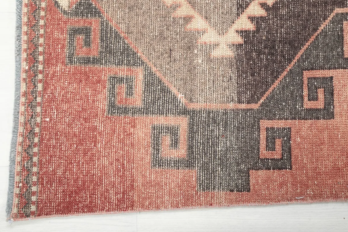 Close-up of the rug's edge, showing the low pile and the subtle color variations in the rust field
