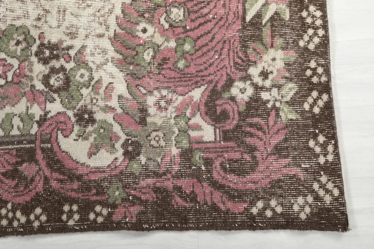 Detail of the brown border with pink and green floral motifs on the vintage rug.
