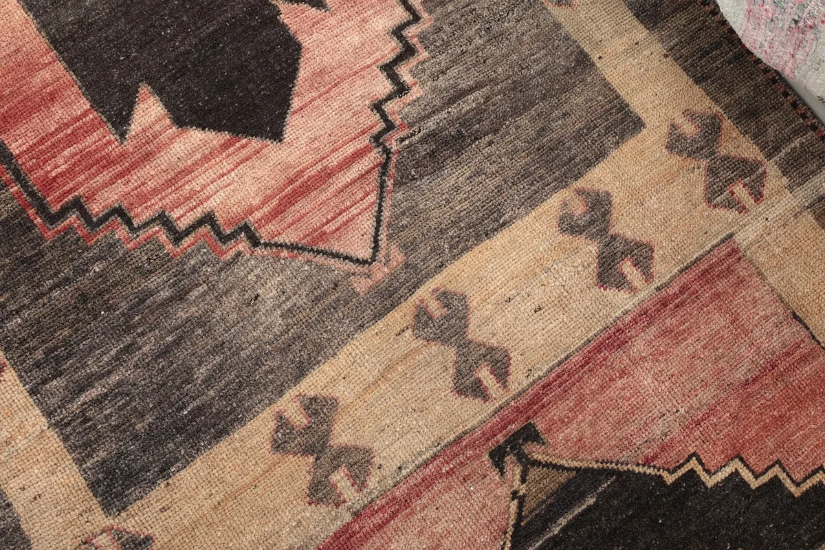 Detailed shot of the hand-knotted wool pile and tribal motifs in rose, gray, and tan