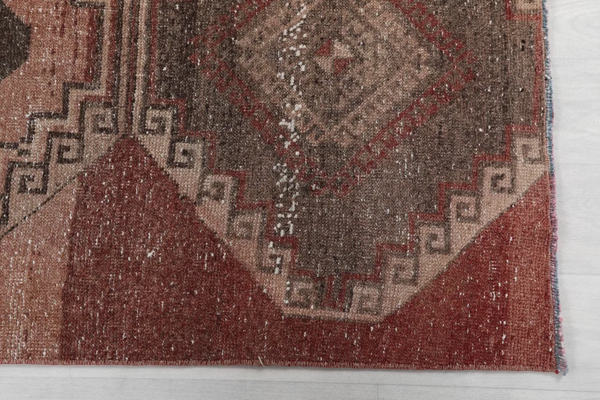 Detailed view of the lower section of the rug, highlighting the rose and rust tones and geometric motifs