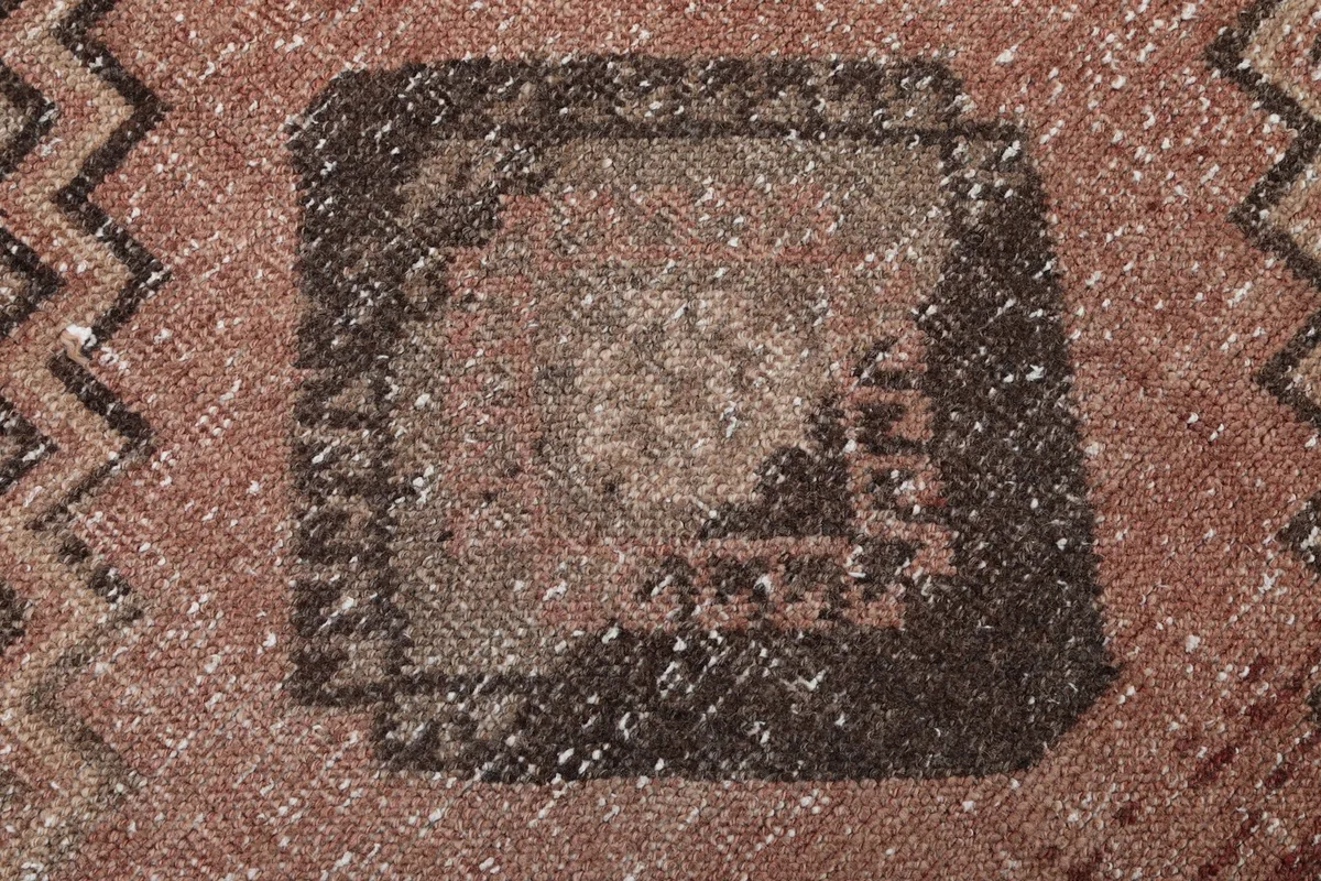 Extreme close-up showing the low pile, wool texture, and distressed character of the rug