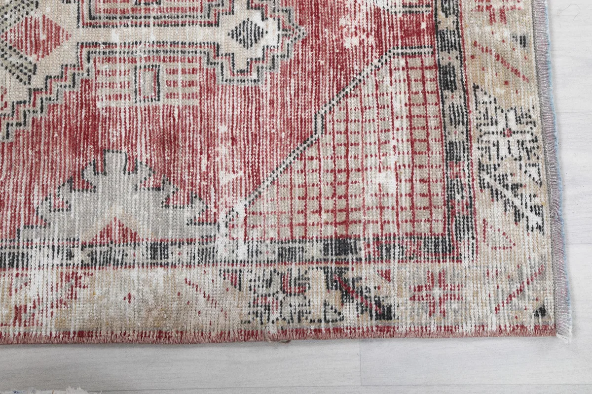 Close-up of the rug's red field and geometric border with visible wear and patina