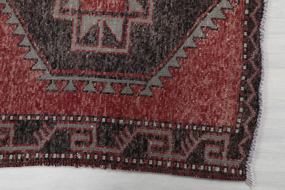 Detailed view of the rug's border and a section of the red field with geometric design.