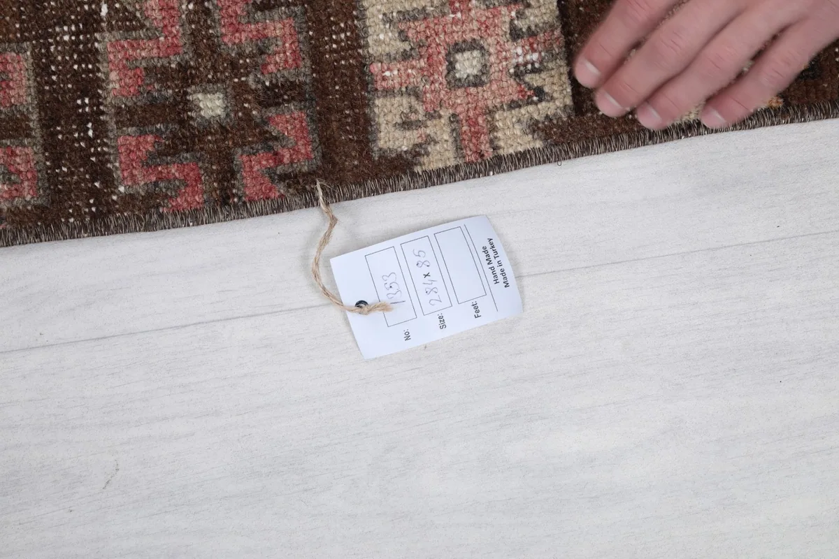 Hand holding a product tag near the edge of the vintage Anatolian runner rug