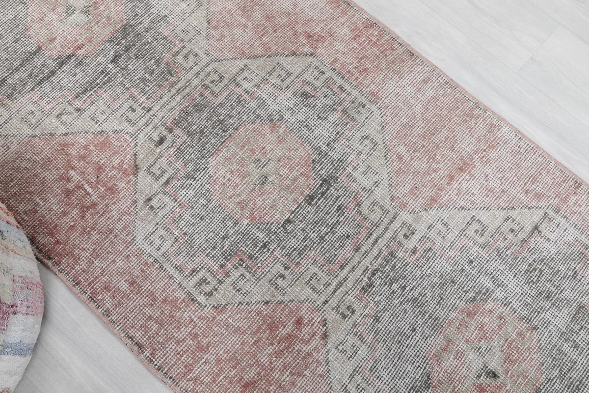 Overhead angle view of the runner rug's central geometric motifs in rose and gray tones.