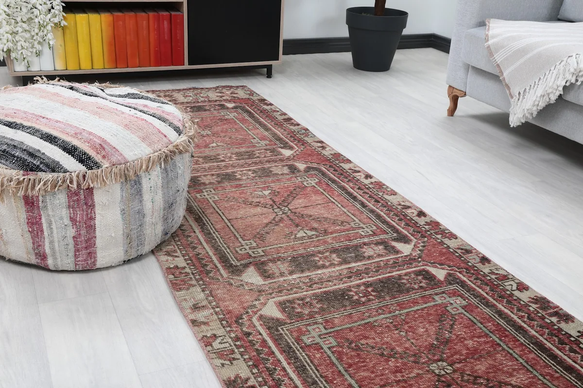 Close-up view of the red runner rug on the floor next to a striped ottoman, showing its texture.