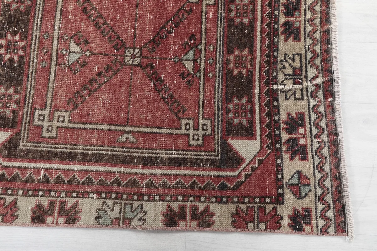 Detailed view of the red rug's corner, showing the geometric patterns and beige border.