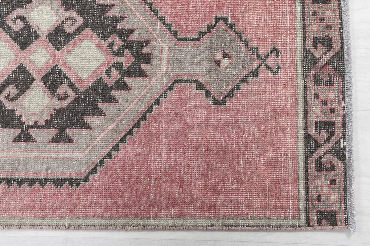 Detailed view of the rose field and gray border with tribal motifs on the vintage runner
