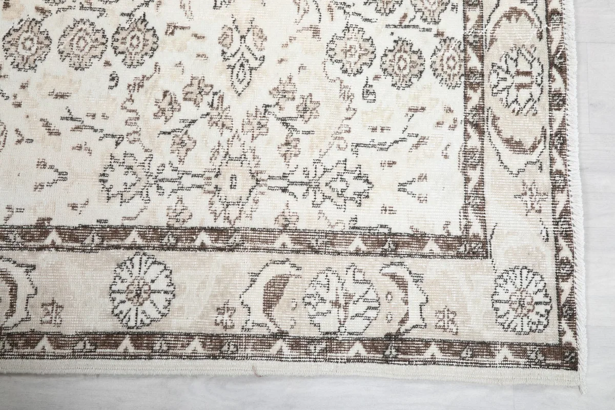 Detailed view of the rug's corner, showing the brown border and ivory field's floral design