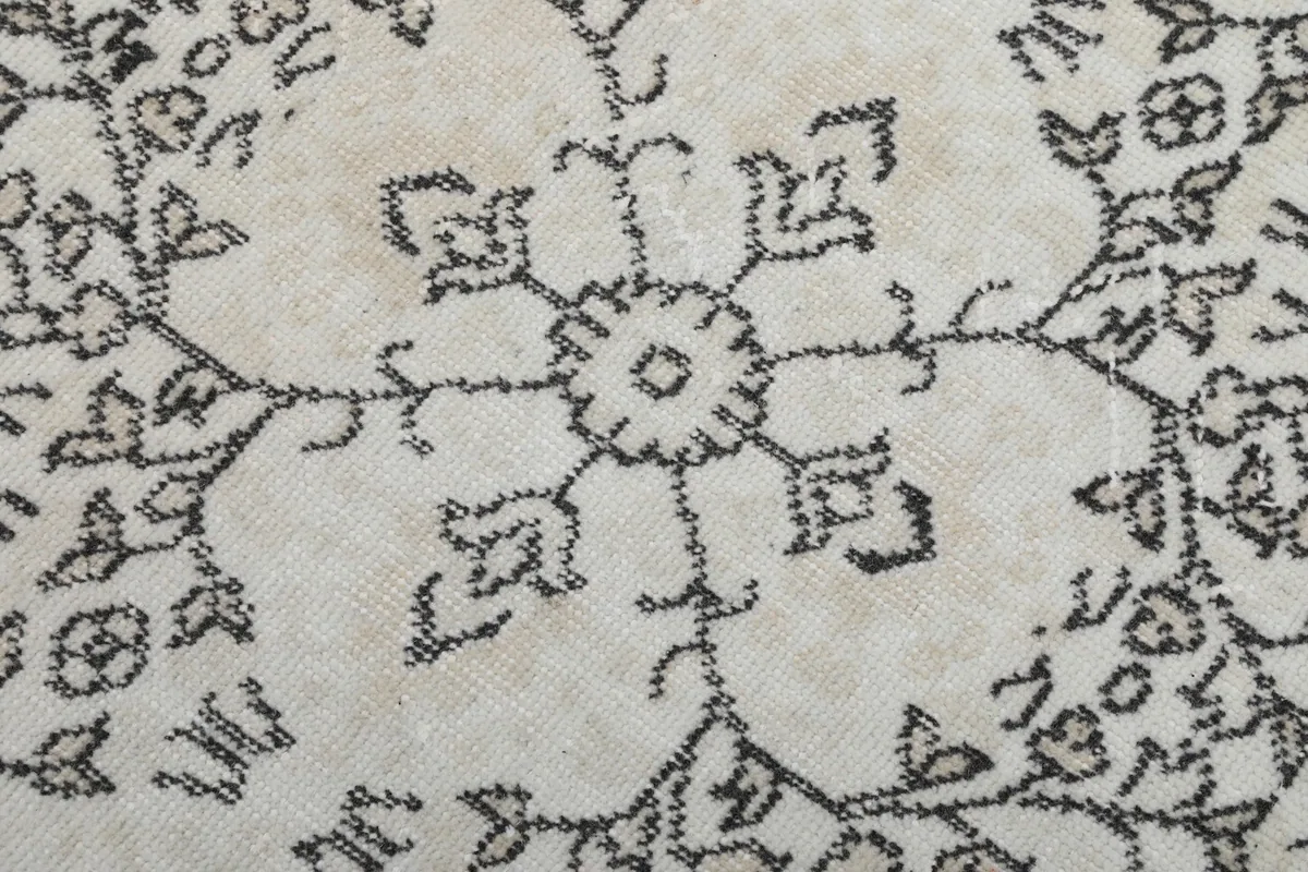 Extreme close-up of a single gray floral medallion motif on the ivory wool pile