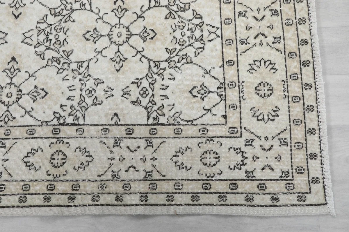 Detail of the rug's border design, featuring intricate gray patterns on an ivory background