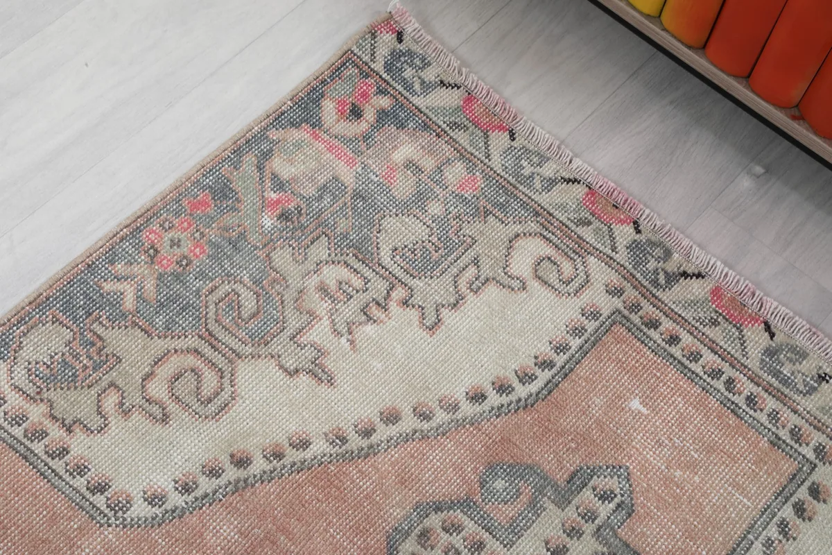 Detail of the rug's border and corner, showing the intricate tribal and floral elements in gray and rose.