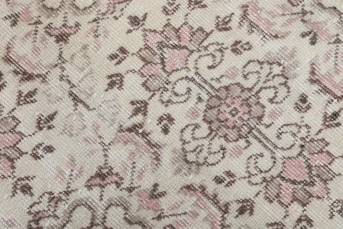 Extreme close-up of the hand-knotted wool pile, revealing the faded rose and brown tones.