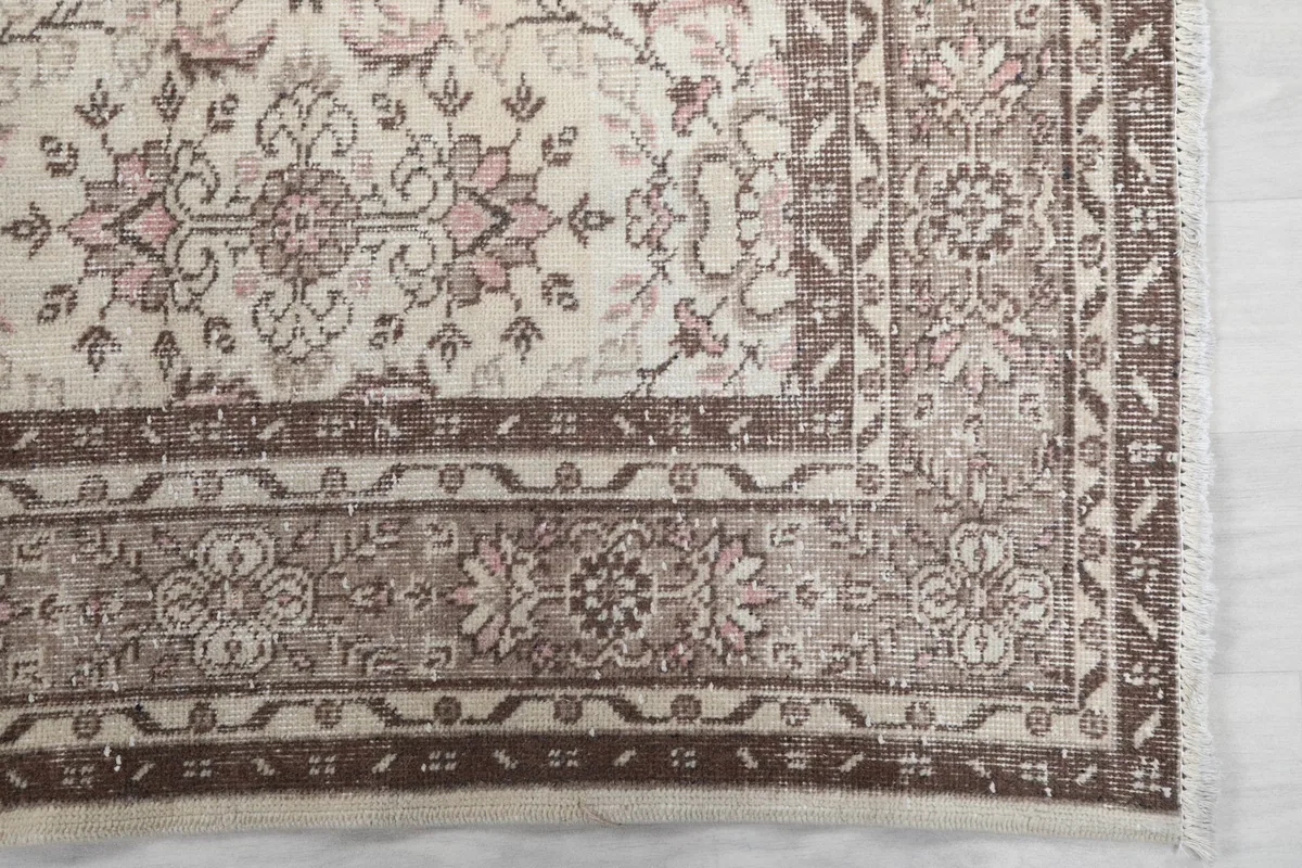 Detail of the rug's brown border and corner, showing intricate patterns and subtle fringe.