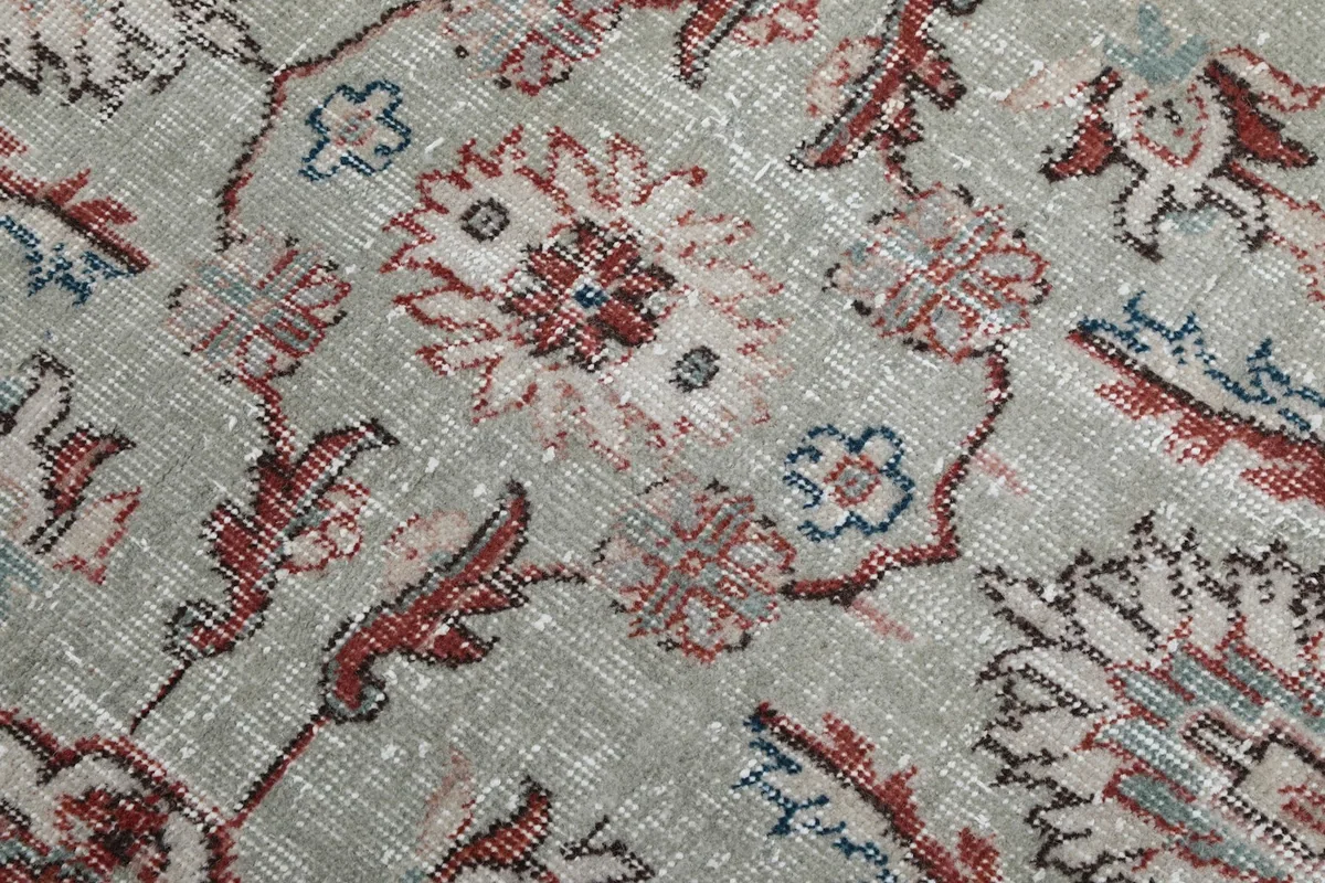 Close-up of the rug's wool pile showing faded red and blue floral motifs