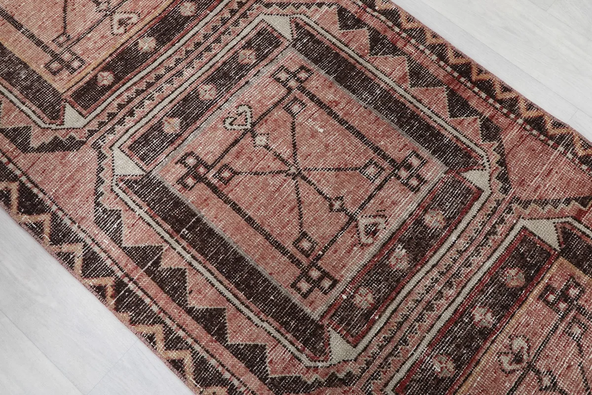 Close-up of a central geometric motif on the rose field, with charcoal and beige accents.
