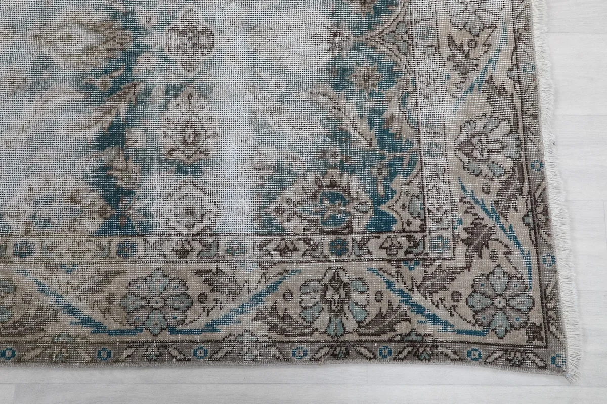 Detail of the rug's border, showcasing a faded floral and geometric design in beige, blue, and brown
