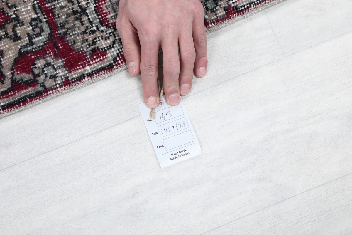 Hand holding a size tag, confirming the dimensions and origin of the rug.