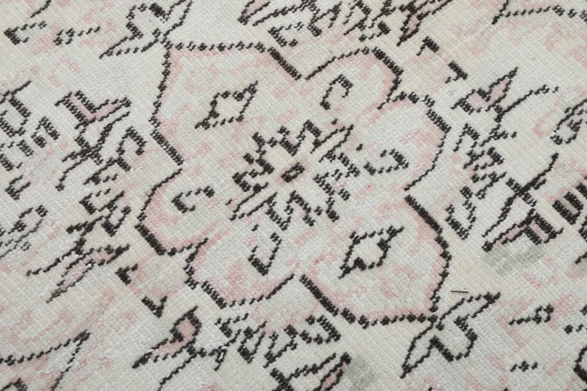 Close-up of the low pile and intricate knotting of the ivory and rose wool fibers.