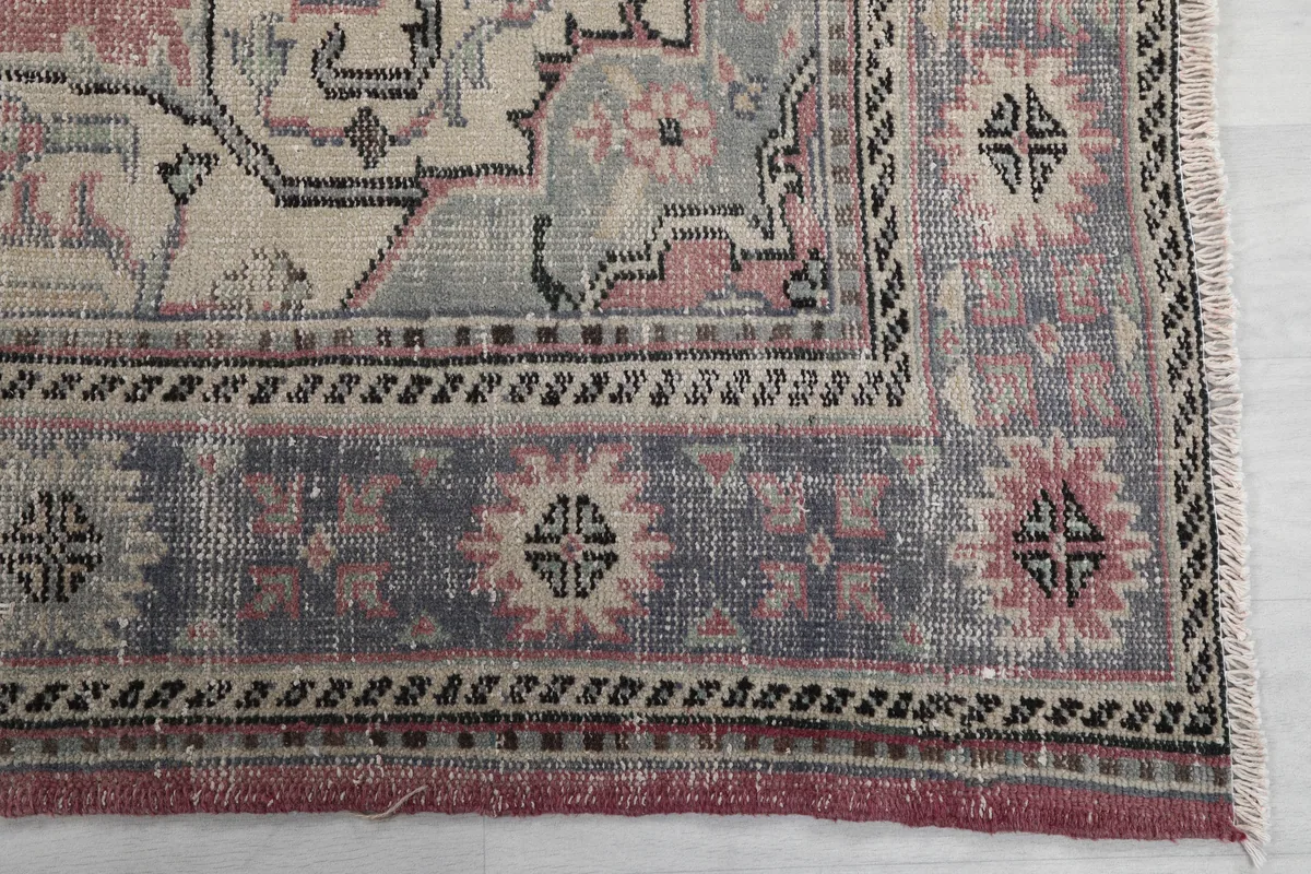 Detail of the rug's gray border with geometric motifs and corner patterns, showing distressed pile.