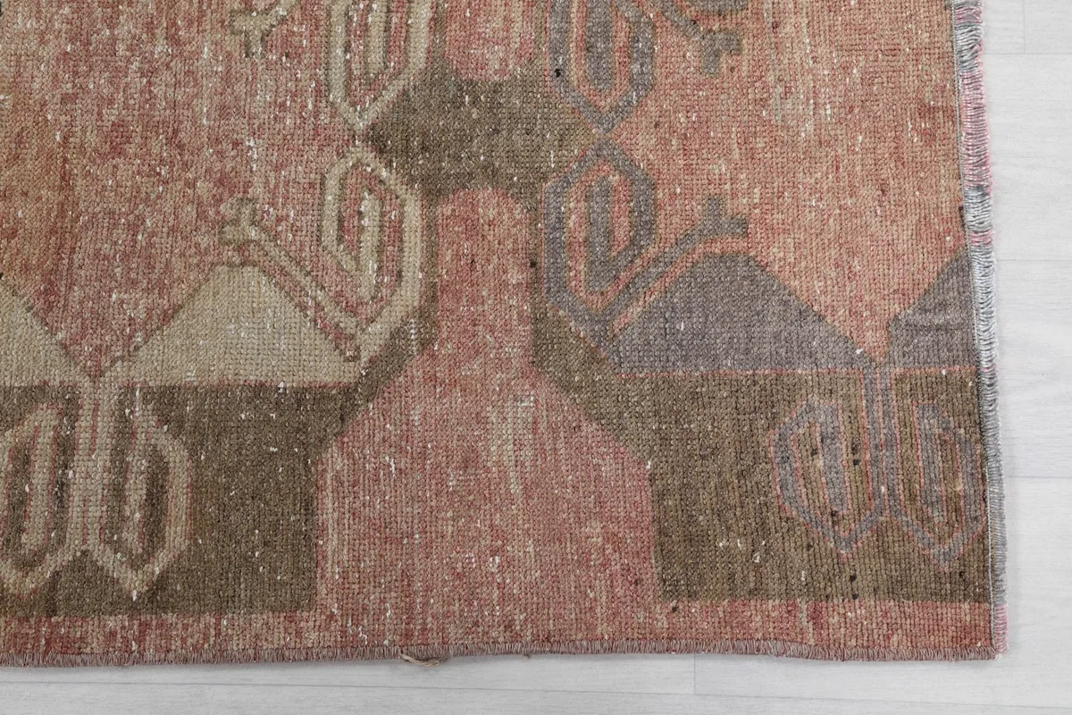 Detailed view of the rug's edge, showing the low pile and intricate geometric design in rose and beige.