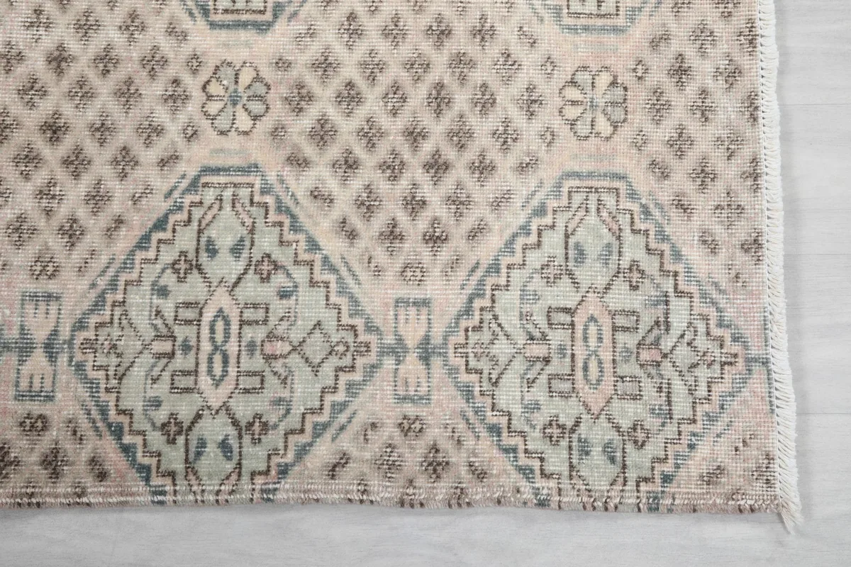 Detailed view of the rug's geometric pattern in gray, rose, and beige, including the edge and fringe.