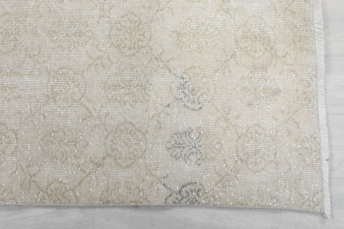 Detailed view of the faded cream and beige floral and medallion motifs on the rug's surface.