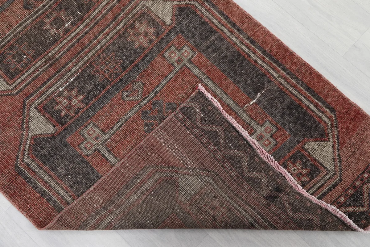 Folded corner of the rug revealing the back of the weave and the rust-colored pile.