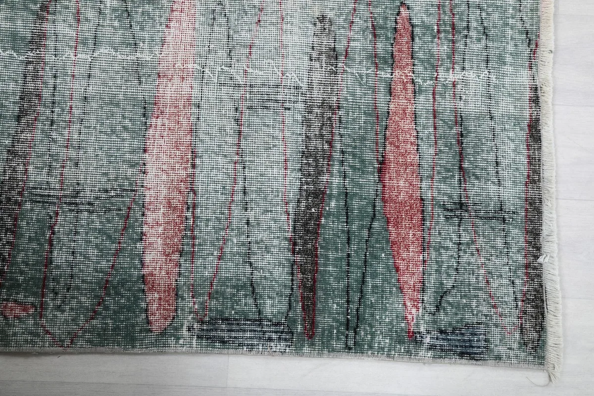 Detail of the rug's edge and abstract rose and charcoal elements on a green background