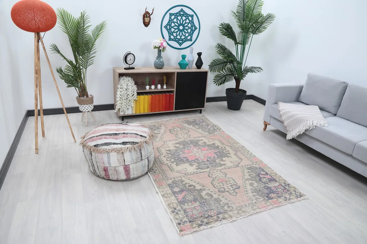 Angle view of the rose and tan rug in a room setting with a round ottoman