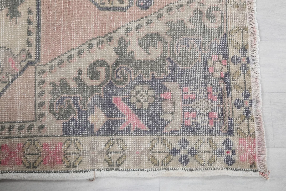 Detail of the rug's border showing faded rose, navy, and tan geometric motifs