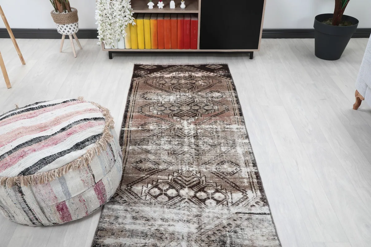 Runner rug viewed from one end in a room, with a pouf and furniture