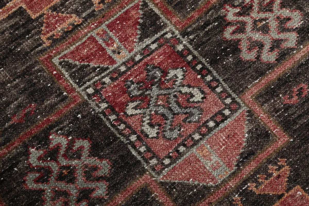 Macro view of the hand-knotted wool pile, showing color variations within the charcoal and rust patterns.
