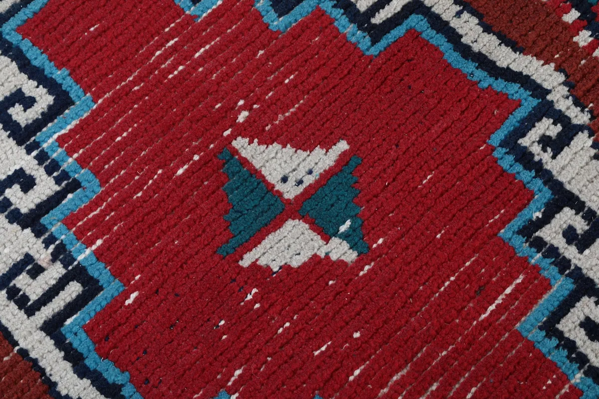 Macro shot of the low wool pile, showing the hand-knotted texture and slight wear in the red and blue sections.
