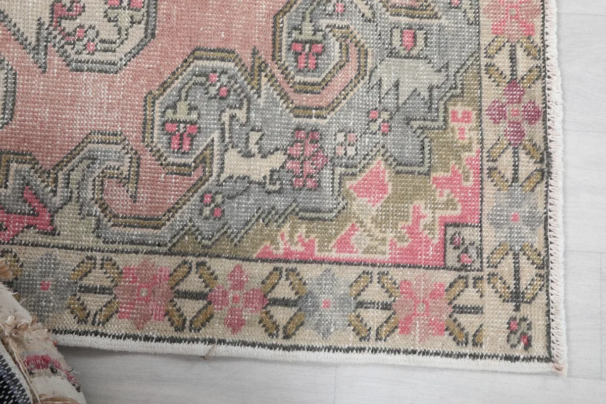 Detailed view of the rug's border and corner motifs in pink, gray, and beige.