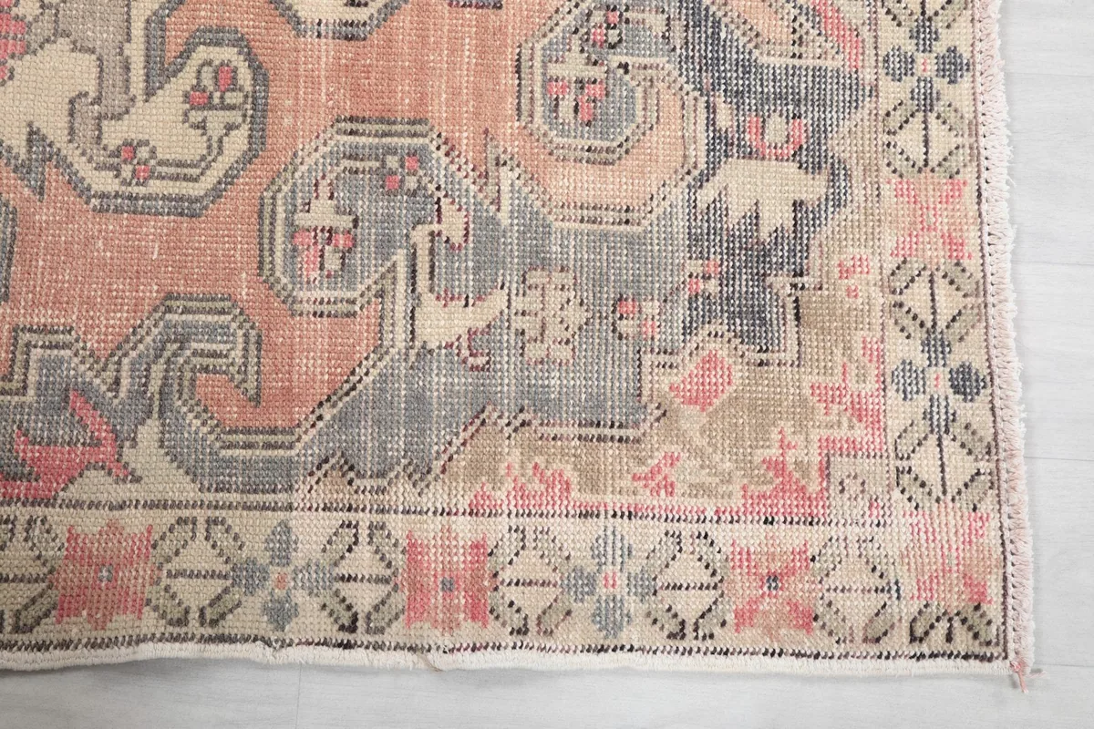 Detailed view of the rug's border and corner with faded rose and gray motifs